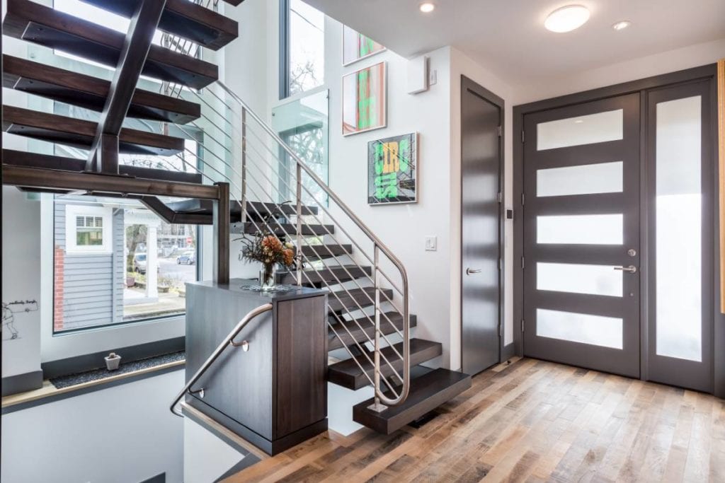 Interior of a modern home with floating staircase, updated doors, hardwood floors, and several windows to illustrate the design build construction process